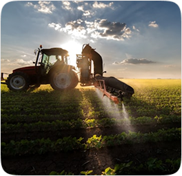 Red tractor spraying crops at sunset